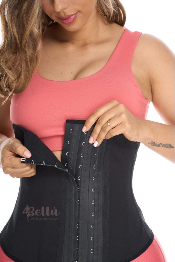 Woman fastening a black latex waist trainer with a front hook-and-eye closure.