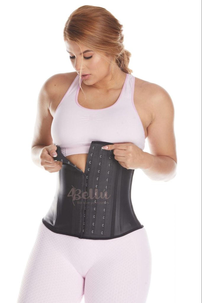 Woman fastening a black latex waist trainer with three rows of hook-and-eye closures.